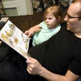 Isä ja tytär lukevat kirjaa sohvalla.