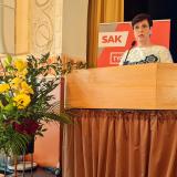 Katja Syvärinen Paasitornin puhujapöntössä pitämässä puhetta, vieressä kaunis kukka-asetelma.