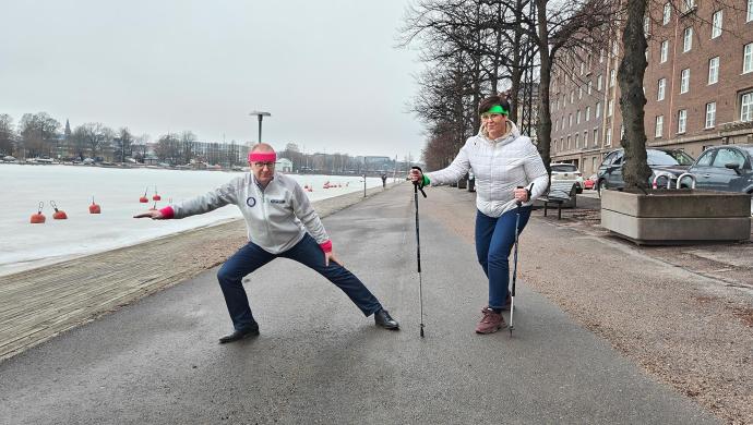 Jarkko Eloranta ja Katja Syvärinen verryttelevät jalkakäytävällä hikipannat päässään, Katjalla lisäksi kävelysauvat.