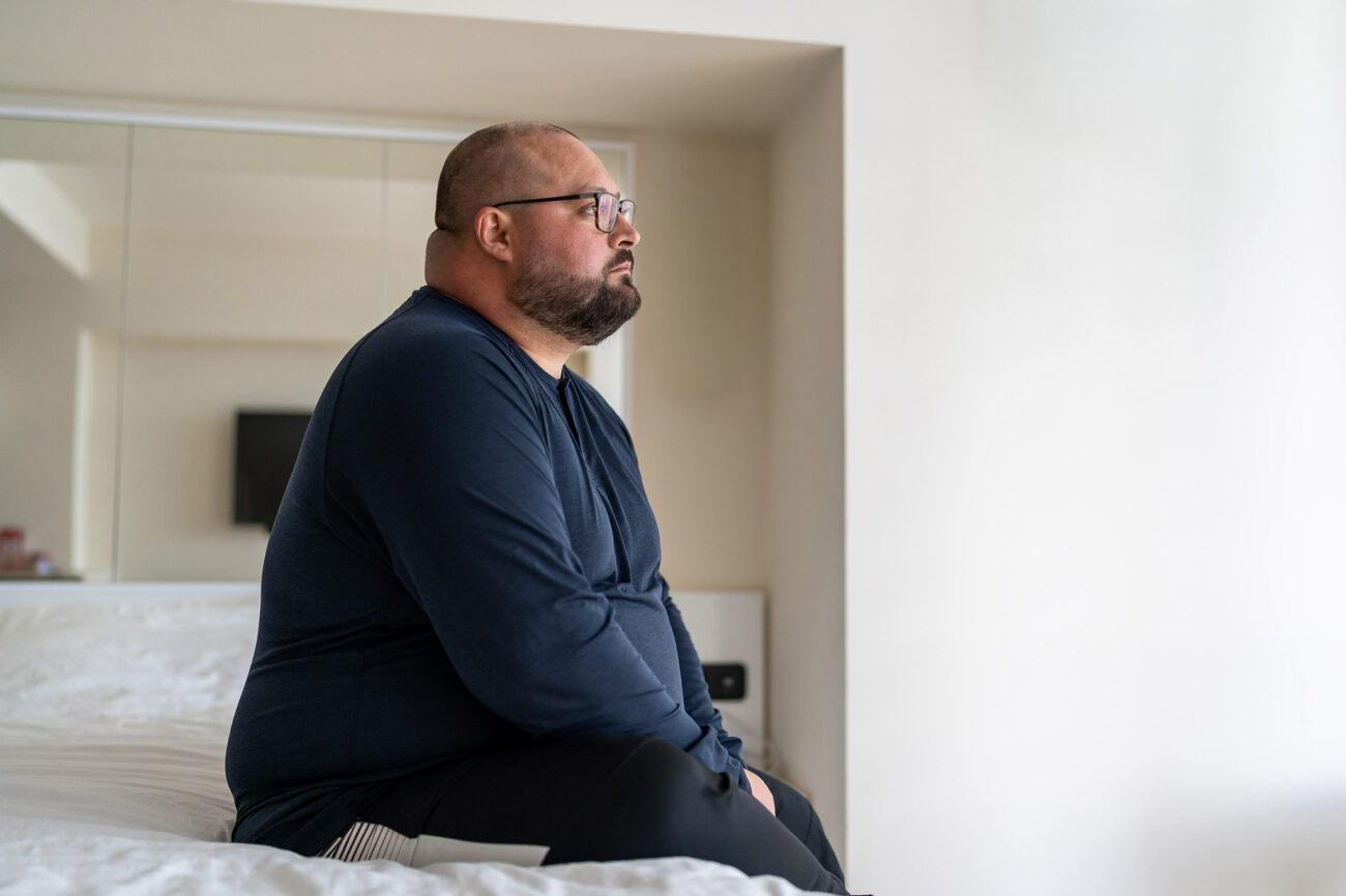 Mies istuu sängyllä ja katsoo tyhjyyteen