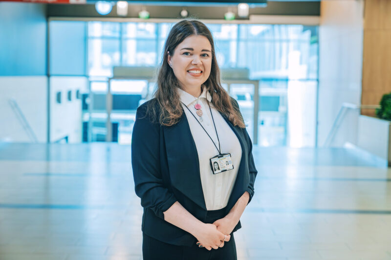 Satu Holm seisoo aulatilassa ja katsoo suoraan kameraan.