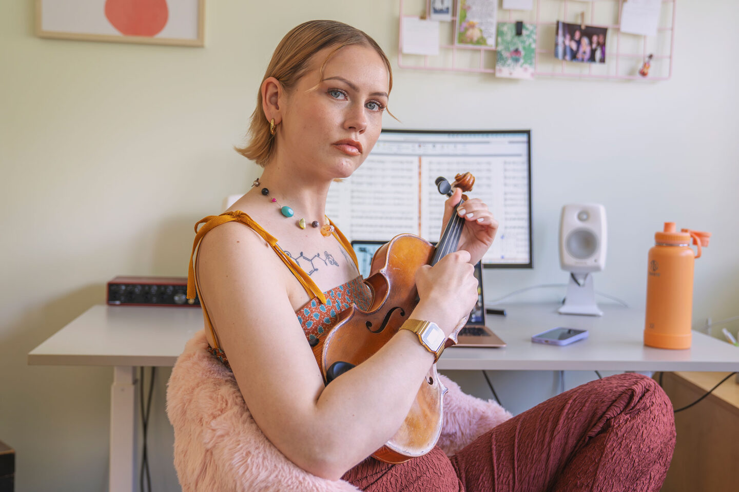 Muusikko-säveltäjä Vilma jää istuu työpöydän tuolilla viulu kädessään ja katsoo suoraan kameraan.
