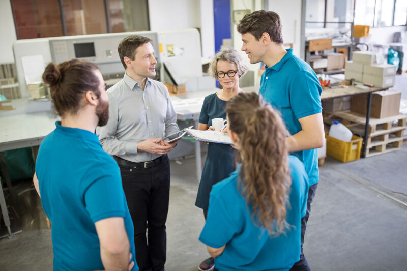 Kirjapainon esihenkilö keskustelee työntekijöidensä kanssa.