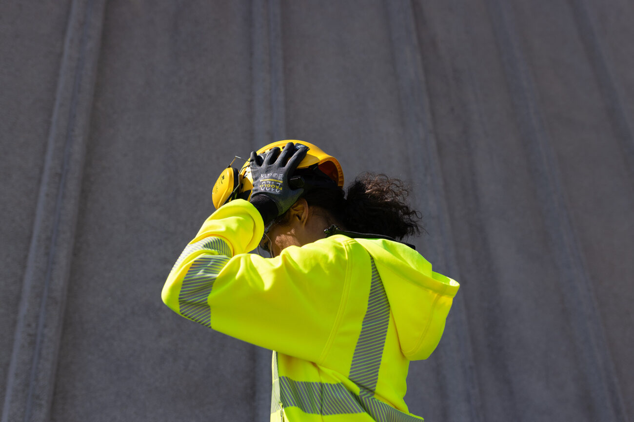 Rakennustyöntekijä pitää kiinni kypärästään.