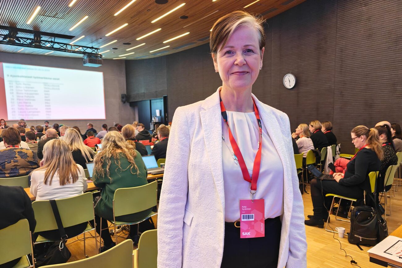 Katja Syvärinen seisoo kokoussalissa, taustalla näkyy edustajiston jäseniä istumassa.