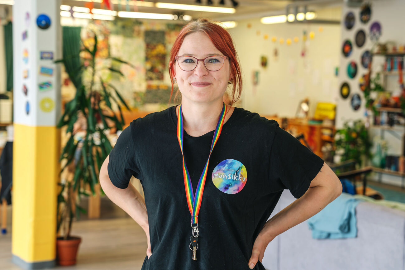 Projektarbetaren Elisa Kivinen står i en färggrant inredd kulturverkstad med händerna i sidan och tittar rakt in i kameran.