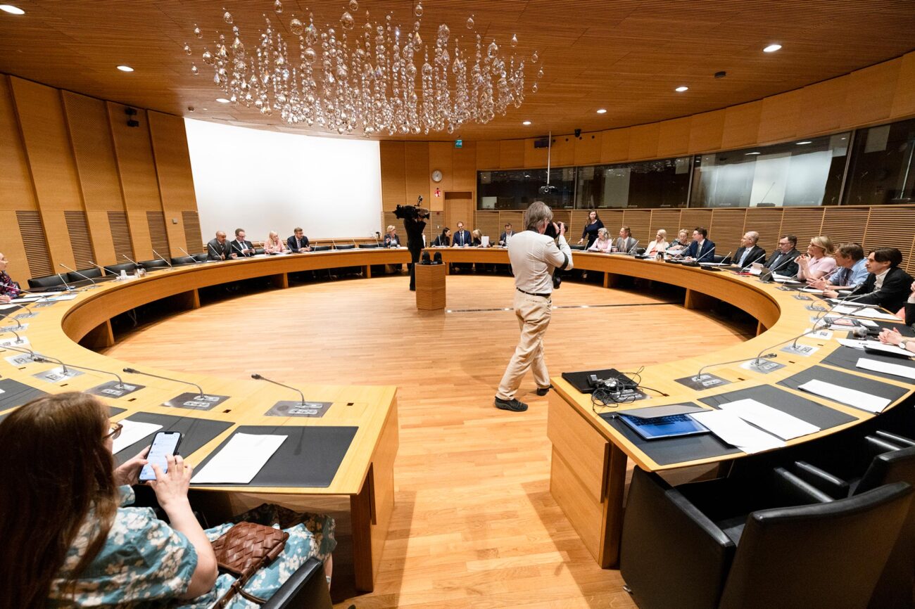 Suuren valiokunnan pyöreä puuverhoiltu sali, jossa pyöreän kokouspöydän ääressä valiokunnan jäseniä ja keskellä valokuvaaja.