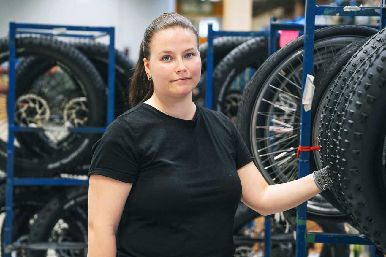 Pyörien kokoonpanija Jenniina Hotti seisoo polkupyörän renkaiden vieressä ja katsoo suoraan kameraan.
