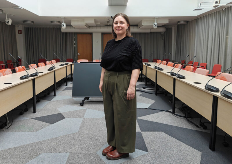 Linnea KIlpeläinen kokovartalokuvassa taustalla kokoushuone.