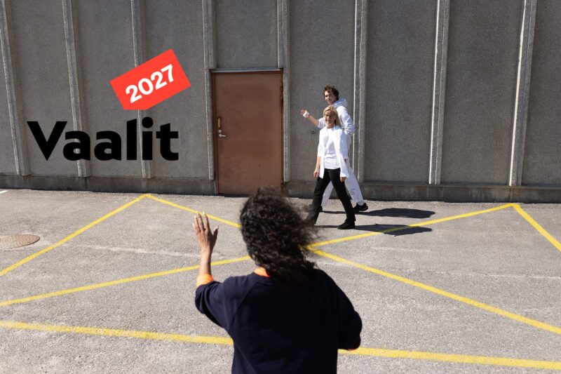 Henkilö seisoo selin kameraan päin ja tervehtii kahta ohikulkevaa työkaveriaan nostamalla käden ylös, kuvan yläkulmassa logo "Vaalit 2027".