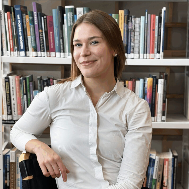 Milla Veteläinen istuu kirjahyllyn edessä.