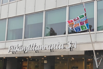 Värikäs kestävän kehityksen lippu liehuu SAK:n keskustoimiston ulkoseinään kiinnitetyssä lipputangossa.