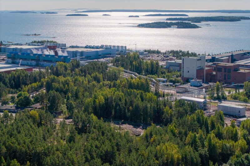 Metsän keskellä iso tehdas, taustalla näkyy merta ja saaria.